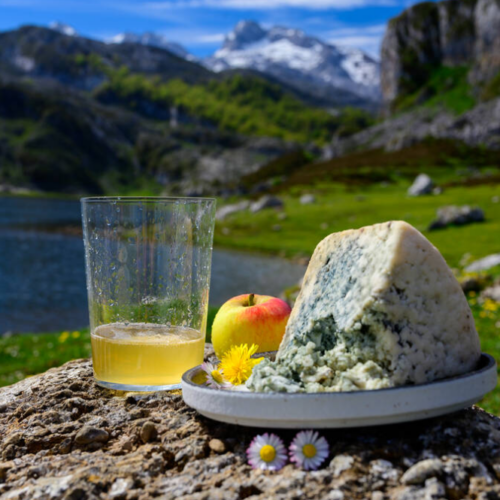 Un culín de sidra asturiana tradicional junto a una ración de queso de Cabrales con los Lagos de Covadonga al fondo