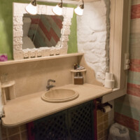 Espejo con marco rústico y lavabo en baño con paredes de piedra blanca