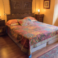 Cama matrimonial rústica con colcha de diseño colorido en la Suite Dalí del Hotel Rural Luna del Valle