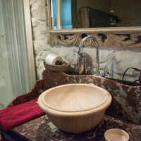 Lavabo tipo bol de piedra rústica sobre encimera de madera en baño con encanto