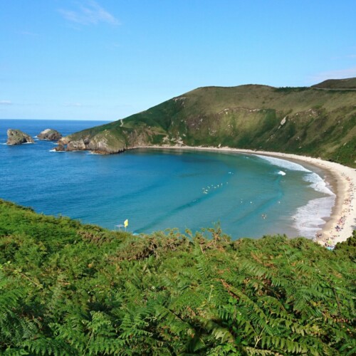 Paisaje de prados verdes y playa de agua turquesa en la costa oriental de Asturias